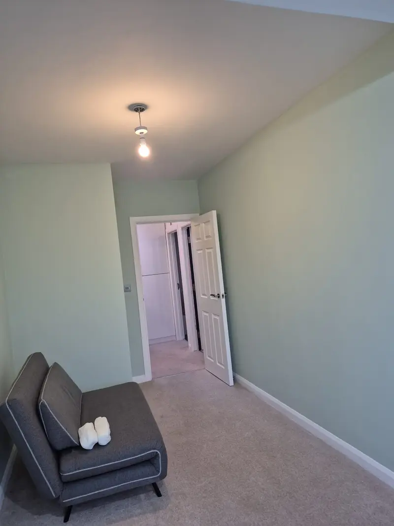 Bedroom freshly painted in soft sage green with white doors and a grey sofa under a pendant light
