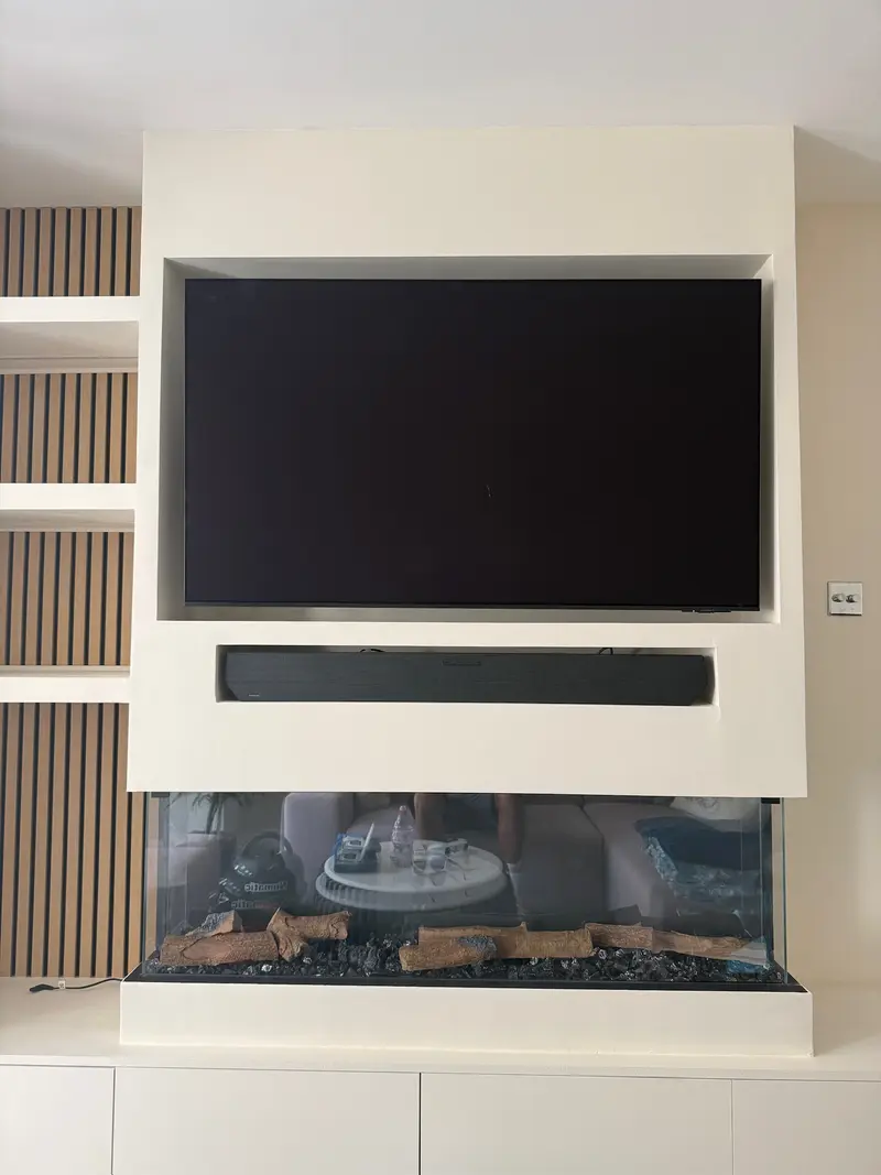 Recessed TV above a soundbar slot and three-sided glass fire, oak slat panelling alongside