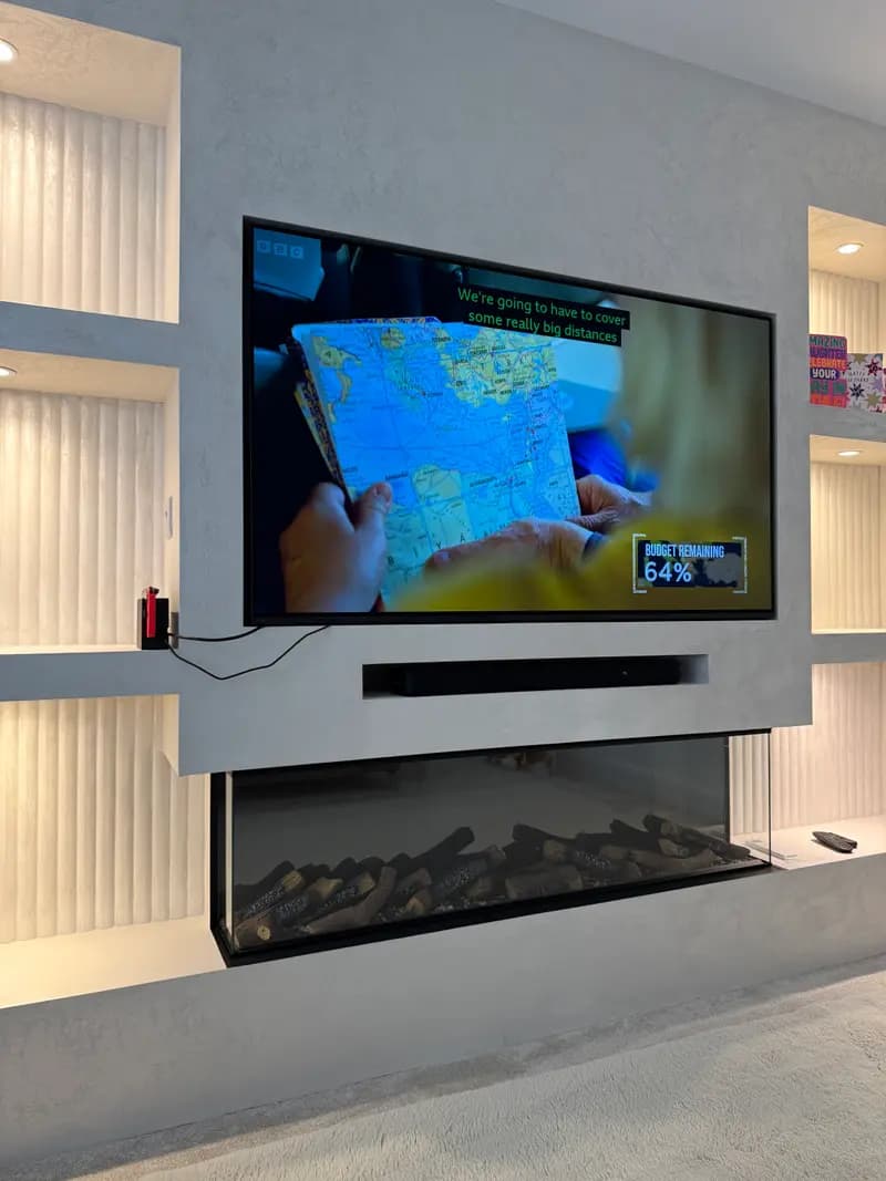 Recessed wall-mounted TV on a grey microcement media wall with fluted LED-lit niches, a concealed soundbar and an inset log-effect electric fire below