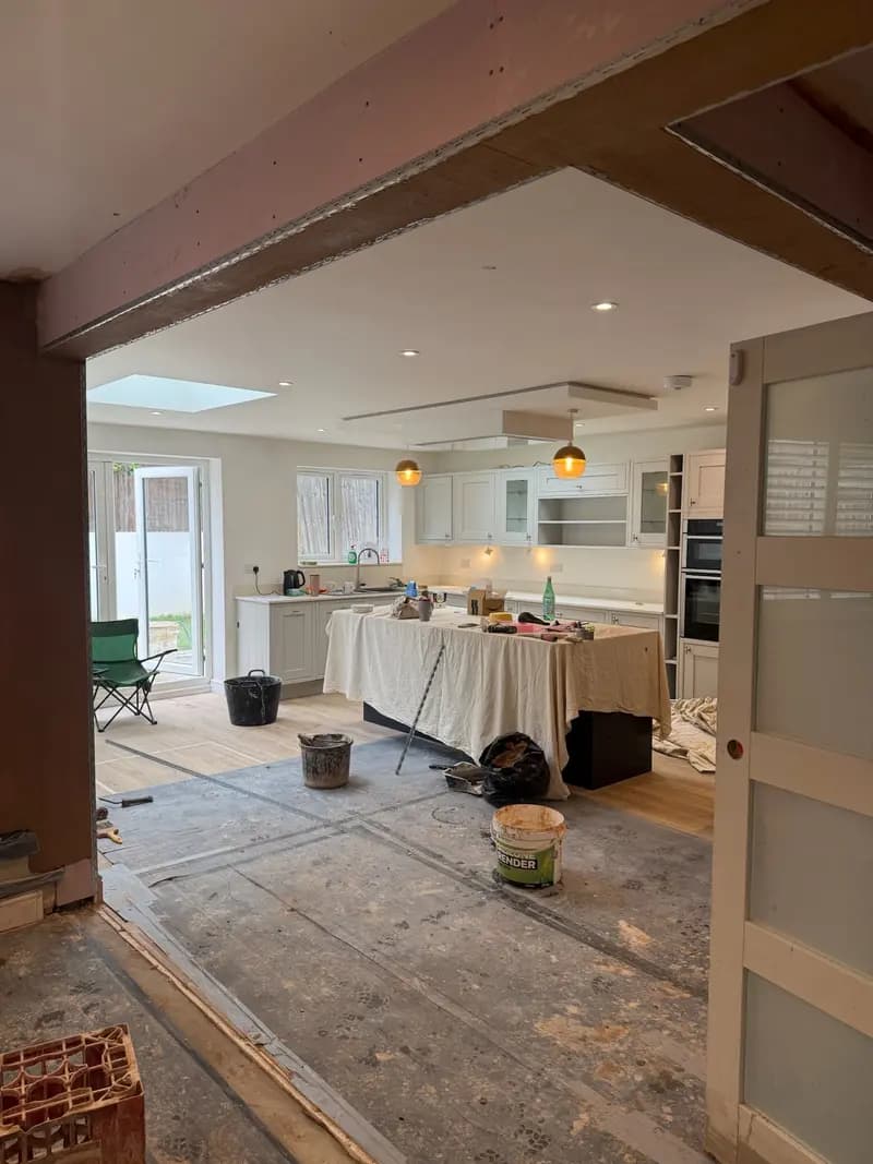 Open-plan kitchen mid-renovation with exposed structural steel beam above and dust sheets over the island