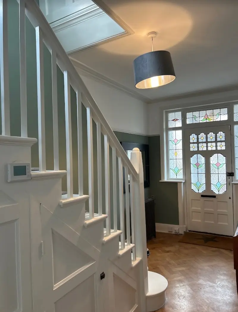 Edwardian hallway with restored stained glass door, parquet floor, white painted staircase against sage green walls