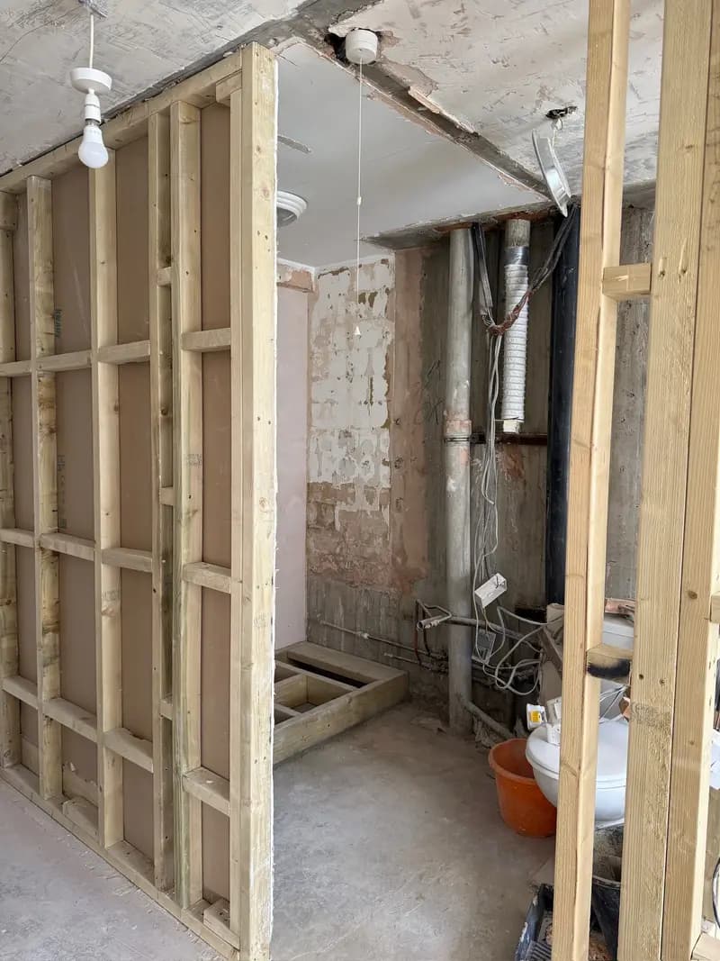Mid-renovation interior showing exposed brick, new timber stud framing, and rough plumbing