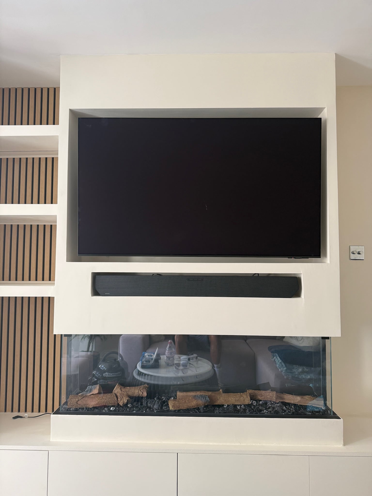 Recessed TV above a soundbar slot and three-sided glass fire, oak slat panelling alongside